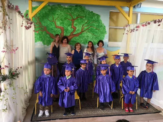 Graduates in purple caps and gowns with their teachers in front of the tree mural