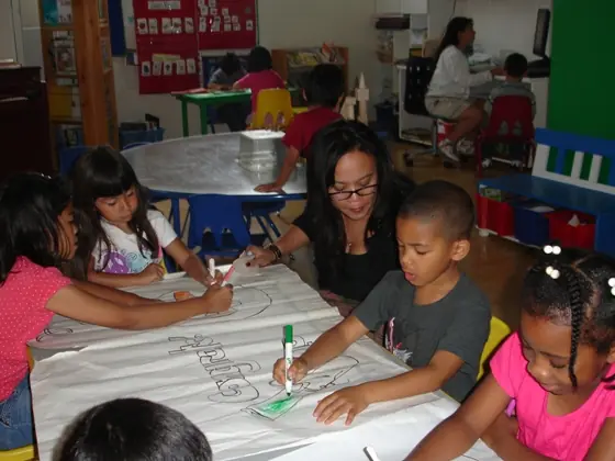 A teacher drawing with children around a long sheet of paper
