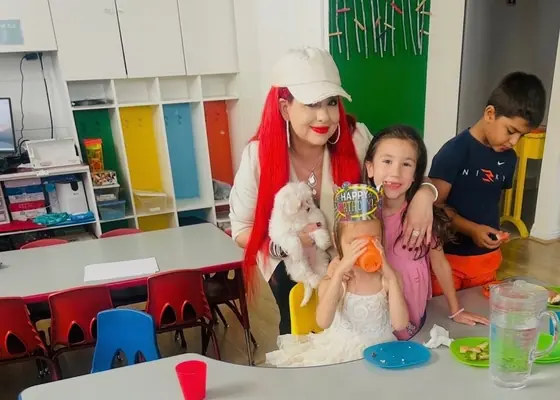 Children at a classroom birthday celebration with an adult holding a white puppy