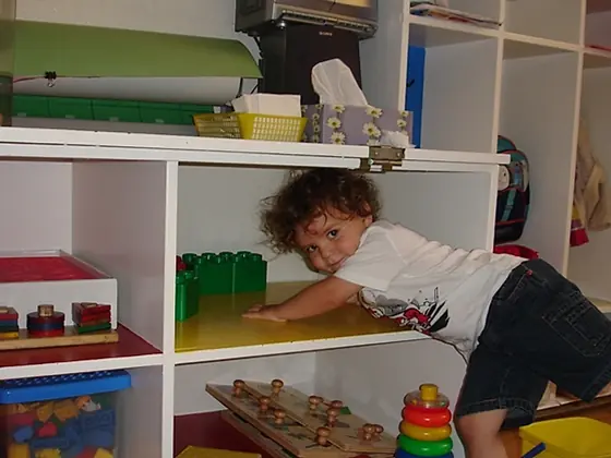 A toddler reaching across a shelf of classroom toys