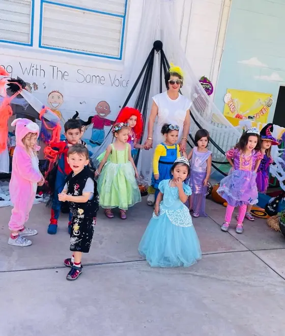 Children in Halloween costumes with a teacher outside the school
