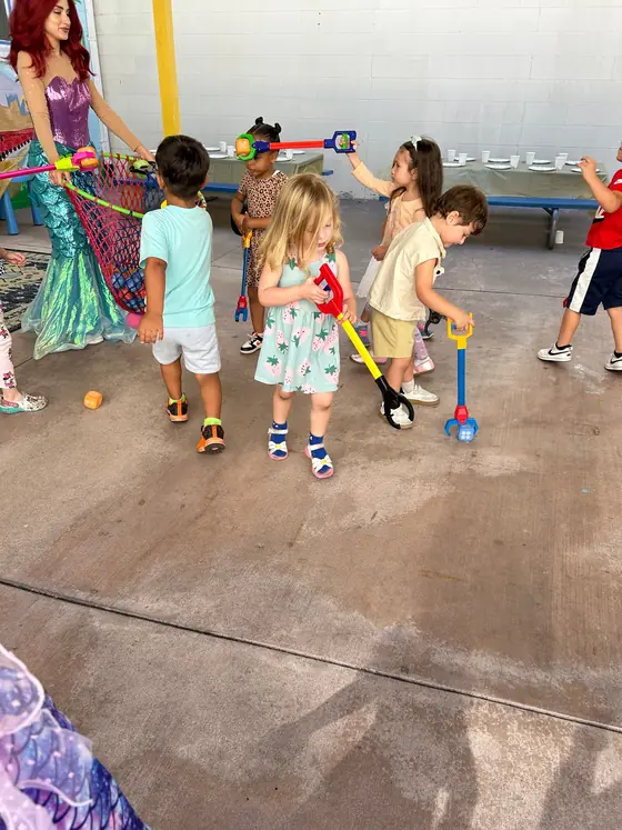 Children playing with toy grabbers beside a performer dressed as a mermaid