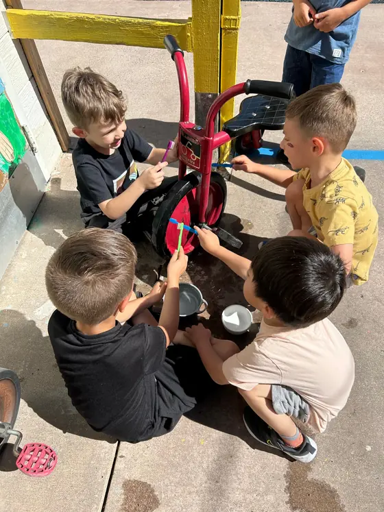 Children scrubbing a tricycle with toothbrushes on the playground