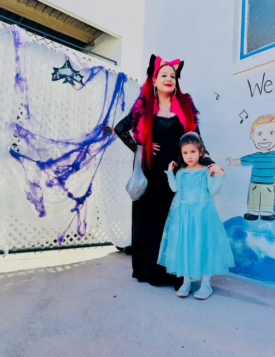 An adult wearing cat ears and a child in a blue dress beside Halloween decorations