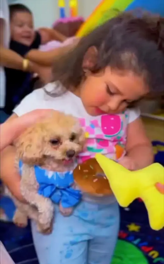 A child holding a small curly-haired puppy at a classroom celebration